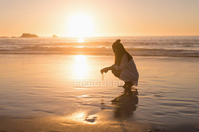Woman crouching in sea water on beach at dusk. — Stock Photo