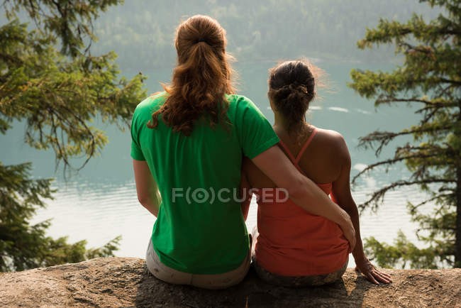 Sportliches Paar, das in der Morgendämmerung nahe beieinander auf einem Felsen sitzt — Stockfoto