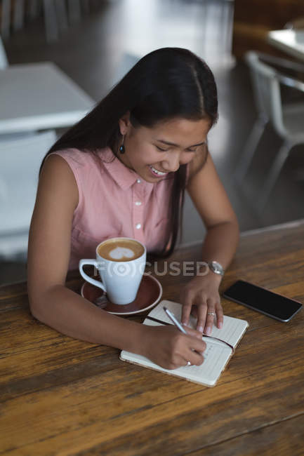 Дівчина-підліток пише на щоденнику в ресторані — стокове фото