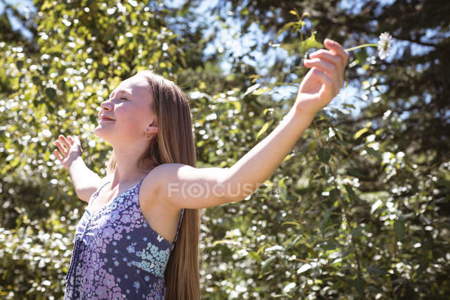 Mädchen breitet Arme auf Feld aus, während sie Blume im Sonnenlicht hält. — Stockfoto