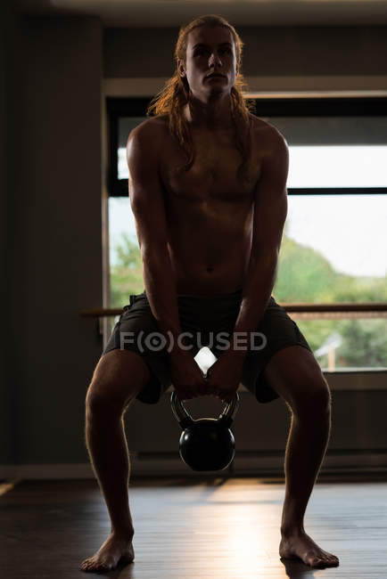 Long-haired man exercising with kettlebell in fitness studio. — Stock Photo