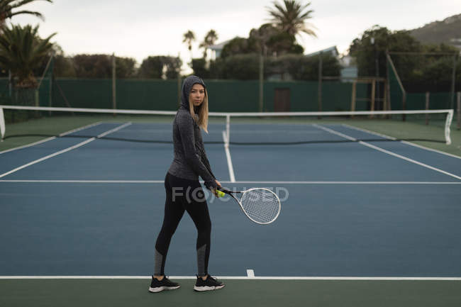 Молода жінка тримає ракетку і тенісний м'яч у тенісному корті — стокове фото