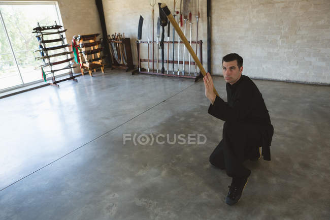 Kung fu fighter practicing with long pole in fitness studio. — Stock Photo