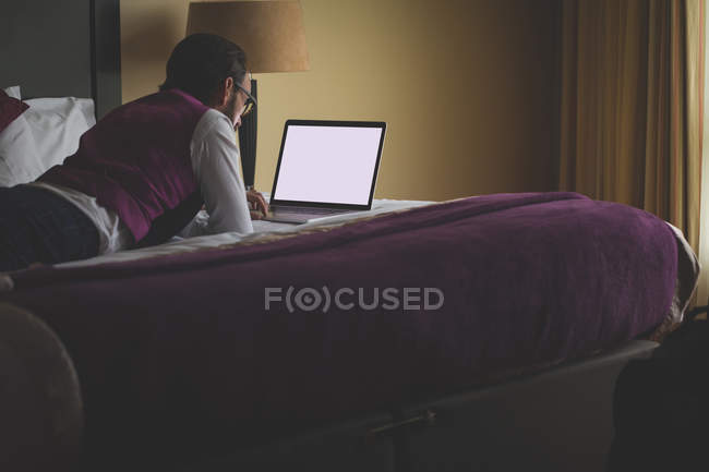 Uomo d'affari che utilizza laptop sul letto in hotel — Foto stock