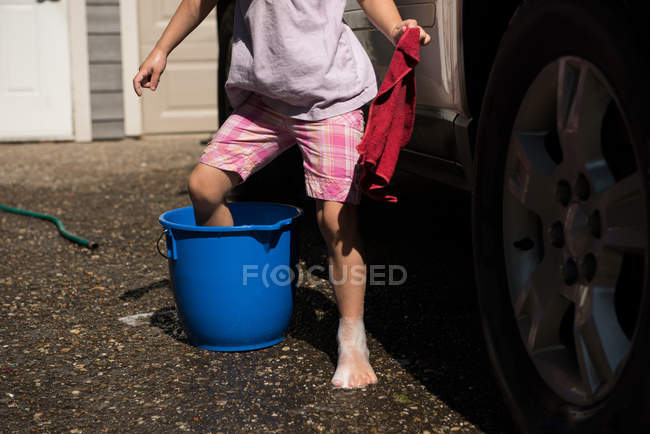 Section basse de la fille mettre sa jambe dans le seau tout en lavant la voiture — Photo de stock