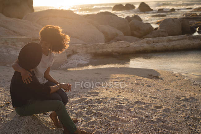 Pareja romántica mirándose mientras están sentados en la playa al atardecer - foto de stock