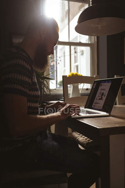 Чоловік сидить на стільці, використовуючи свій ноутбук вдома — стокове фото