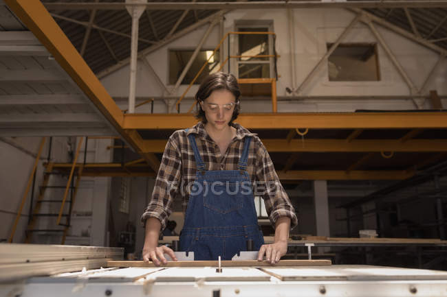 Young craftswoman measuring wooden piece in workshop. — Stock Photo