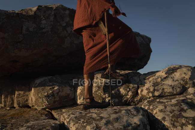 Maasai man in traditional clothing walking on rock at countryside — Stock Photo
