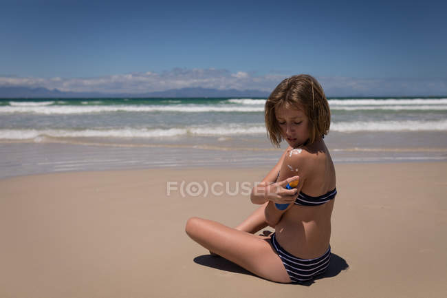 Ragazza adolescente che applica crema solare lozione sul retro in spiaggia — Foto stock