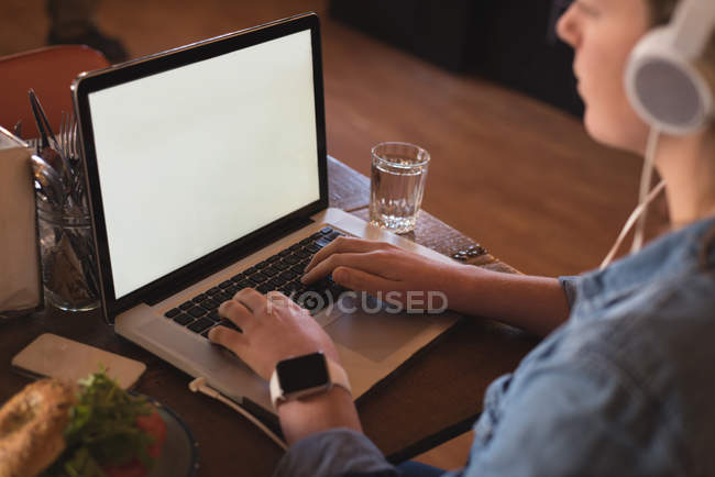 Woman listening music while using laptop at table in cafe — Stock Photo