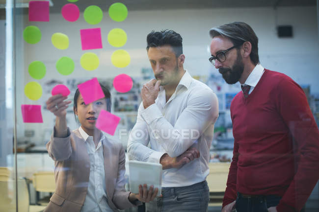 Business executives discussing over sticky notes in office — Stock Photo