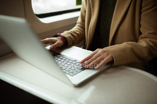 Primer plano de la mujer joven de pelo rojo usando su computadora portátil en tren - foto de stock