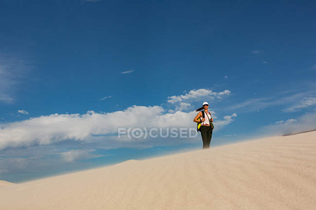Senderista femenina con mochila de pie sobre arena en un día soleado - foto de stock