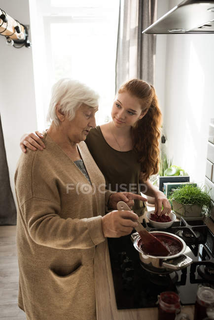 Grandmother and grand daughter cooking raspberry jam in kitchen at home — Stock Photo