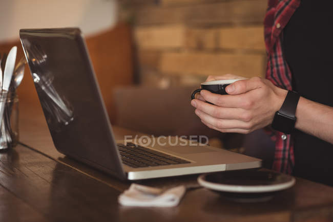 Sección media del hombre usando el ordenador portátil mientras toma café en la cafetería - foto de stock