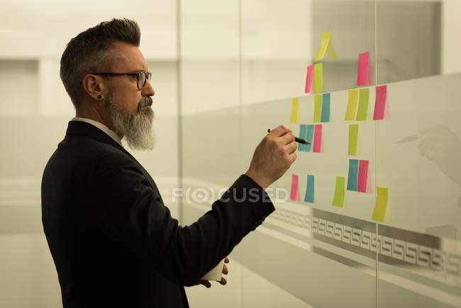 Ejecutivo de negocios escribiendo en notas adhesivas en la oficina - foto de stock