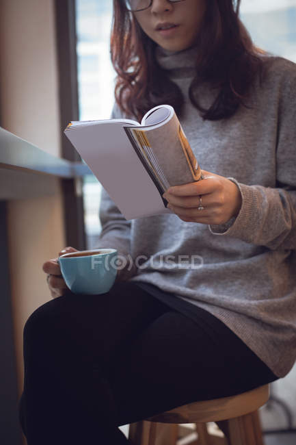 Milieu de la section de la femme de lecture magazine tout en prenant un café à la cafétéria — Photo de stock