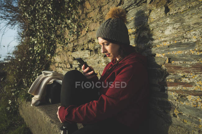 Woman using mobile phone against stone wall outdoors. — Stock Photo