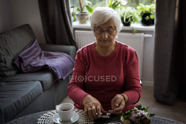 Старша жінка дивиться на ліки у вітальні вдома — стокове фото
