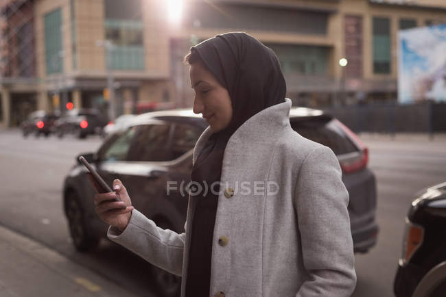 Femme dans le hijab en utilisant le téléphone mobile sur la rue de la ville — Photo de stock
