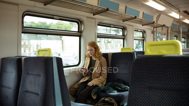 Червоне волосся молода жінка використовує свій мобільний в поїзді — стокове фото