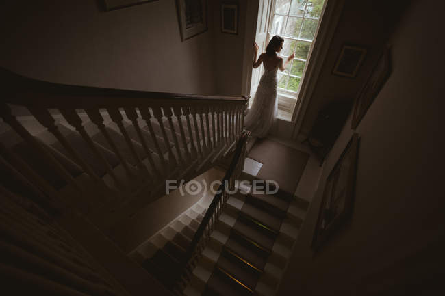 Visão traseira da noiva em pé na janela em casa — Fotografia de Stock
