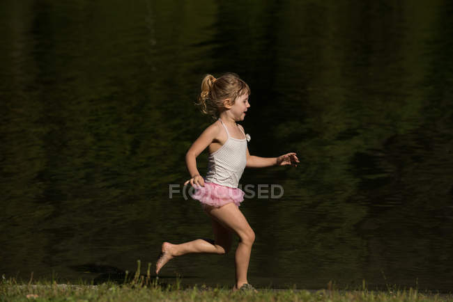 Linda chica corriendo cerca de la orilla del río en un día soleado - foto de stock