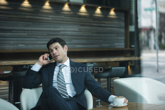 Empresario hablando por teléfono mientras toma un café en el hotel - foto de stock