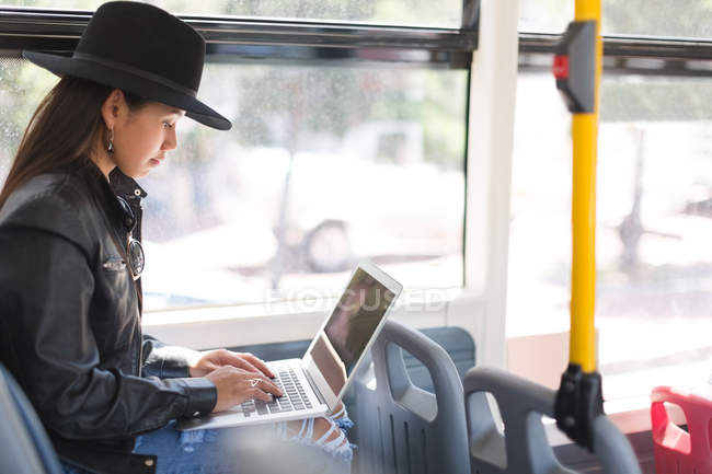 Vista lateral de la chica adolescente utilizando el ordenador portátil en el autobús - foto de stock