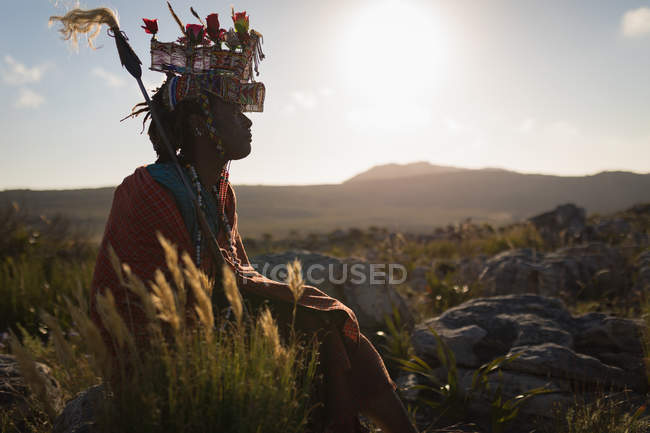 Hombre masai con ropa tradicional sentado en el campo en un día soleado - foto de stock