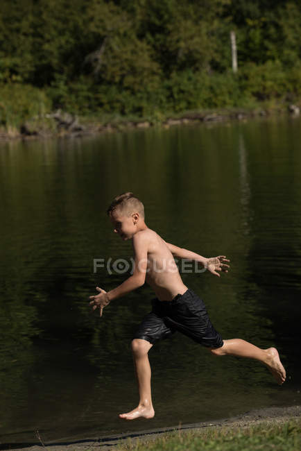 Беззаботный мальчик бежит возле берега реки в солнечный день — стоковое фото