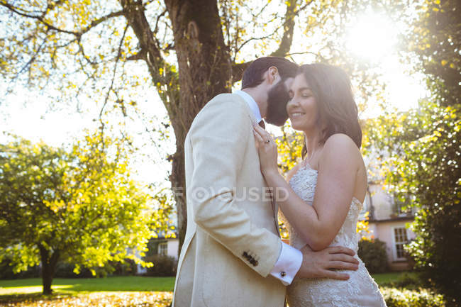 Lächelndes Brautpaar, das sich an einem sonnigen Tag im Garten umarmt — Stockfoto
