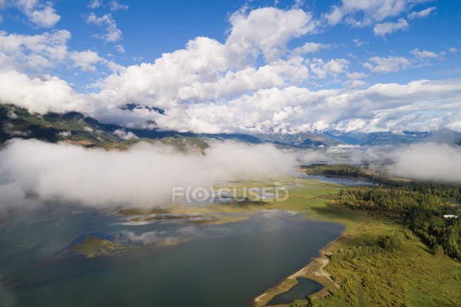 Schöne Aussicht auf weiße Wolken über dem See inmitten grüner Landschaft — Stockfoto