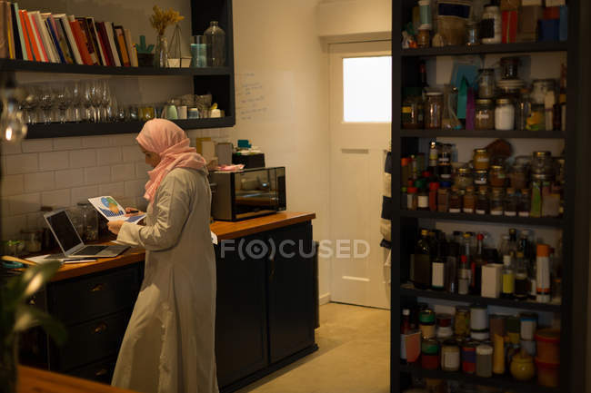 Muslim woman looking at the printout in kitchen at home — Stock Photo