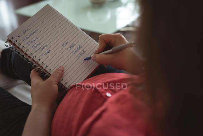 Беременная женщина пишет в блокноте дома — стоковое фото