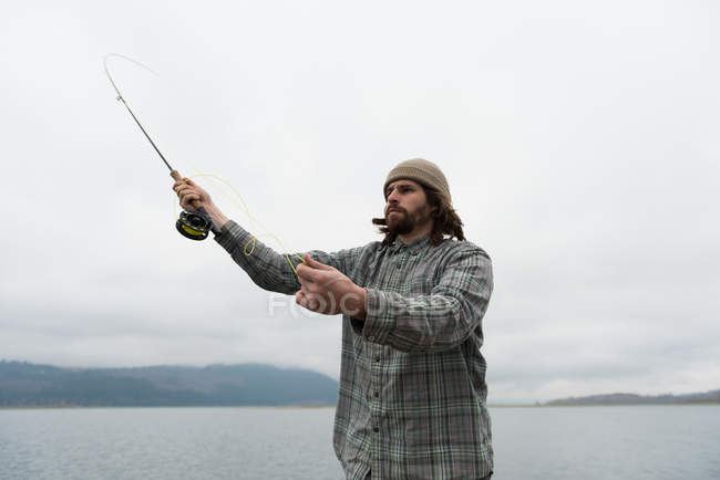 Homem jogando linha de pesca no rio em um dia nebuloso — Fotografia de Stock