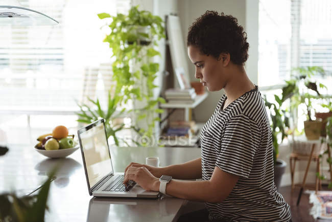 Вид збоку жінки, що працює на ноутбуці, маючи каву — стокове фото