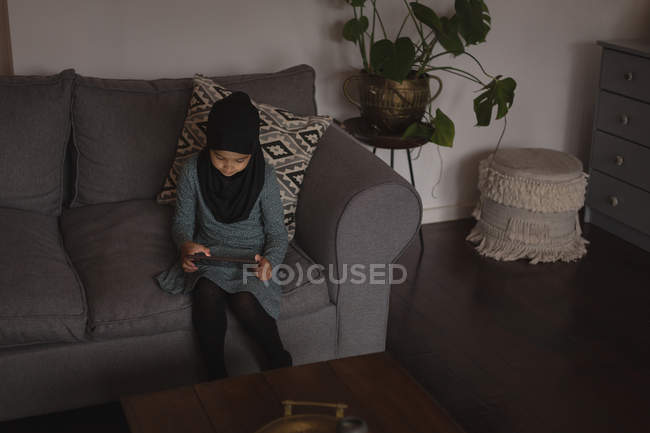 Muslim girl sitting on sofa and using digital tablet at home — Stock Photo