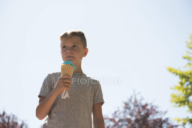Задумчивый мальчик ест мороженое в солнечный день — стоковое фото