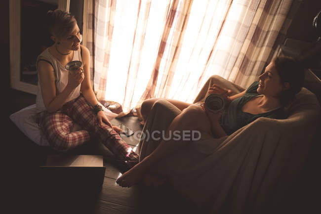 Jovens mulheres interagindo com xícaras de café em casa . — Fotografia de Stock