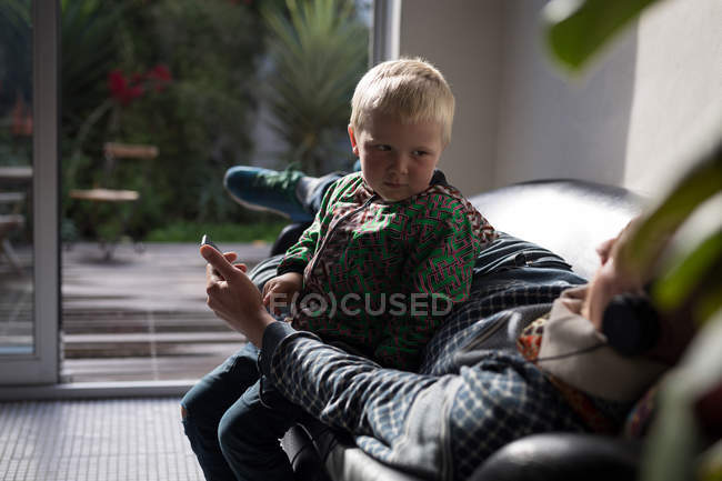 Son looking as father listening music while resting on sofa in living room. — Stock Photo