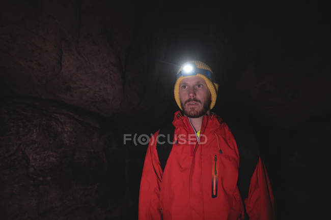 Hiker standing inside the dark cave wearing head torch with backpack — Stock Photo