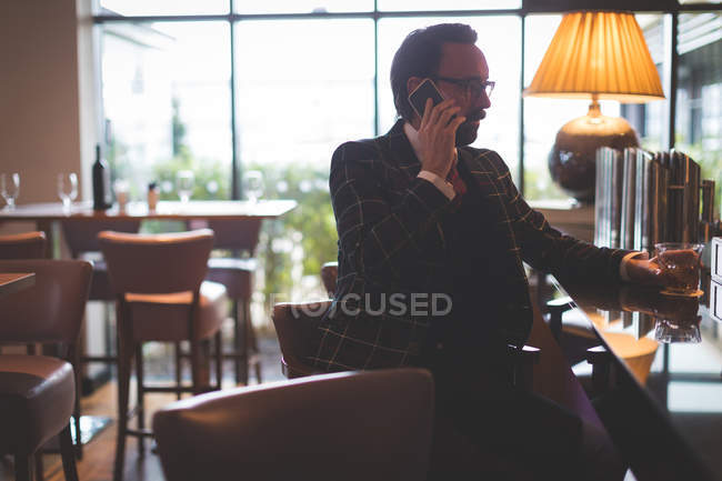 Homme d'affaires parlant sur un téléphone portable tout en ayant du whisky dans le bar — Photo de stock