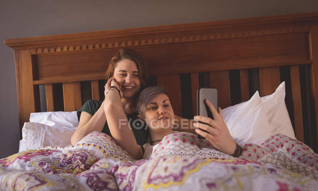 Лесбийская пара делает селфи в постели дома . — стоковое фото