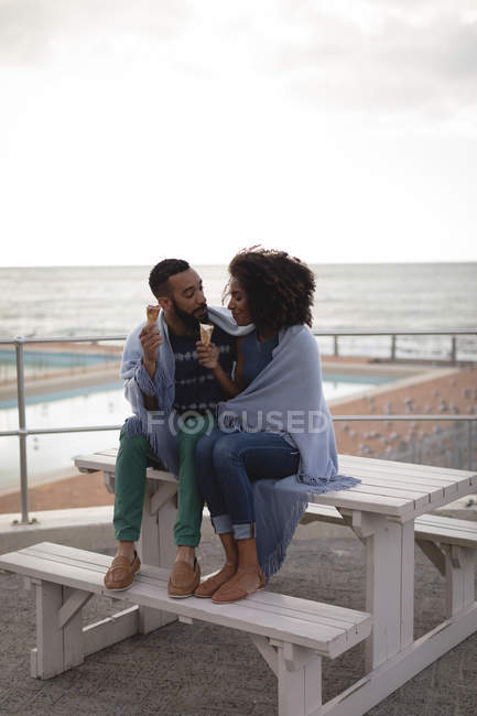 Couple wrapped in a shawl having ice cream at dusk — Stock Photo