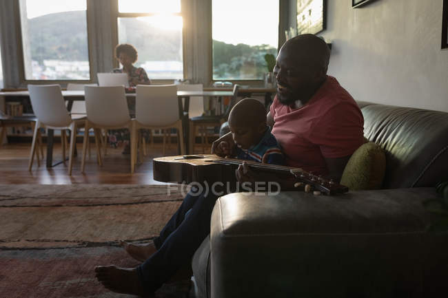 Vater und Vorschulsohn spielen zu Hause im Wohnzimmer Gitarre. — Stockfoto