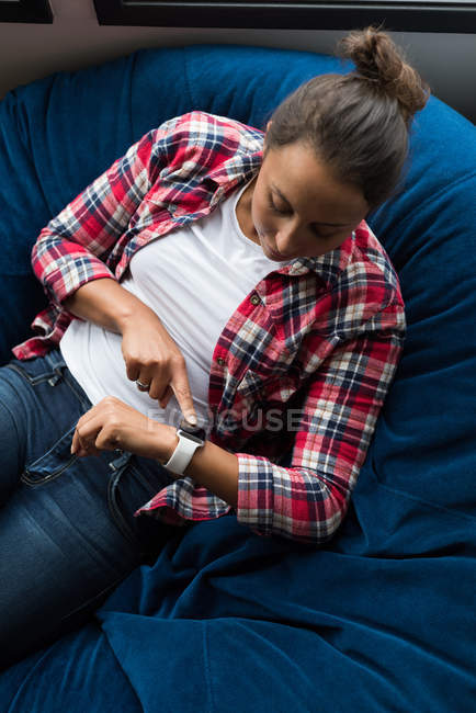 Female executive sitting on arm chair and using smartwatch in office — Stock Photo