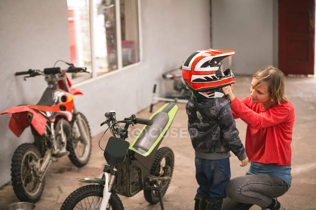 Madre preparando a su hijo para montar en bicicleta en el garaje - foto de stock