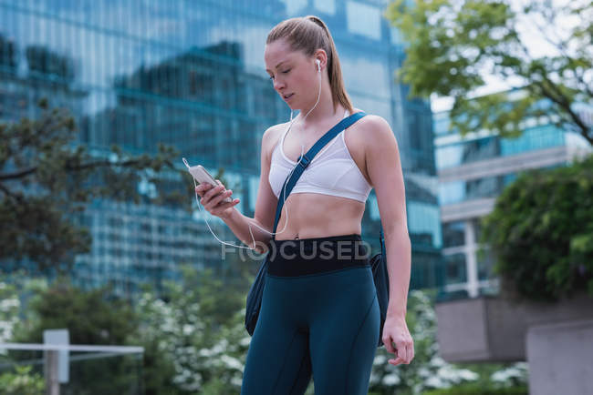 Jovem mulher esportiva usando telefone celular na rua — Fotografia de Stock